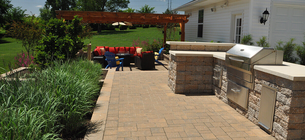 Pergola with seating area and built-in grill in backyard.