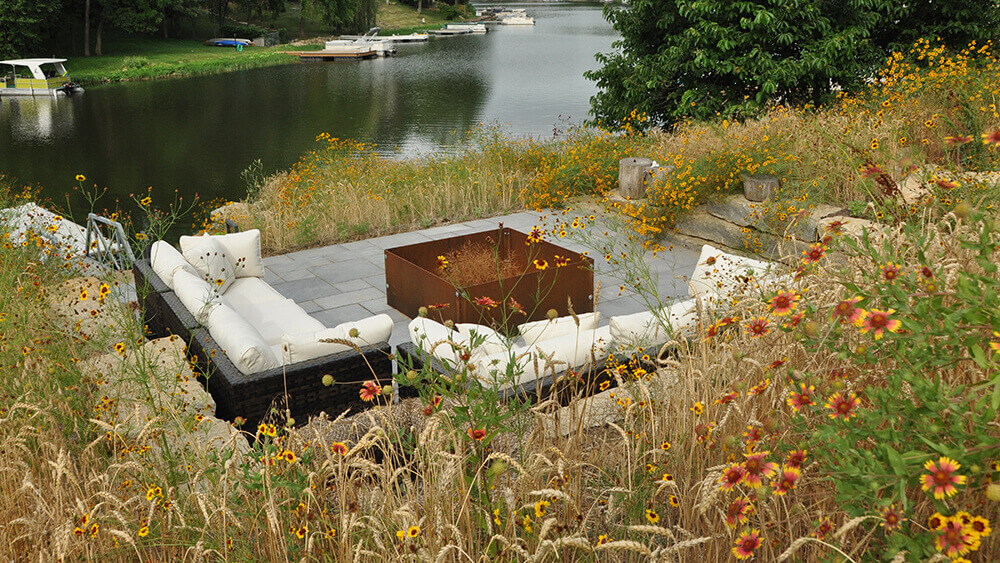 fire pit with seating area surrounded by fall wild flowers and overlooking water