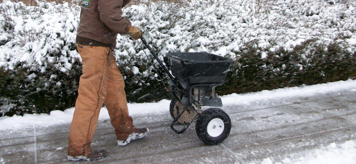 Employee removes snow and treats sidewalks with salt for ice control.